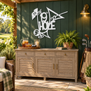 White 19th Hole metal wall art on a forest-green outdoor golf patio with teak drinks cabinet and plants