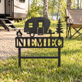 Campsite Custom Metal Sign in Black hammered powdercoat, personalized with NIEMIEC and planted beside a travel trailer at a wooded campsite.
