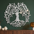 Celtic Tree of Life wall art in polished metal with directional grinding marks on a forest-green wall above a walnut sideboard.