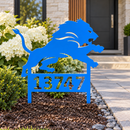 Detroit Lions custom address metal yard art in Honolulu Blue with cutout numbers planted beside a landscaped stone-and-cedar house entrance.