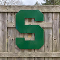 Weather-resistant green metal block S sign attached to a rustic gray cedar fence.