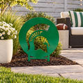 Green Michigan State Spartans helmet logo metal yard art with buried stakes beside a football-themed backyard patio and white flowers.