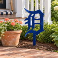Old English D Metal Yard Art in Navy Blue with a buried center stake, displayed beside a cottage porch and coral flowers.