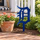 Old English D Metal Yard Art in Navy Blue with a buried center stake, displayed beside a cottage porch and coral flowers.