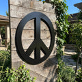 Full view of peace symbol metal wall art mounted outdoors, showcasing size, placement, and protective coating in natural sunlight.